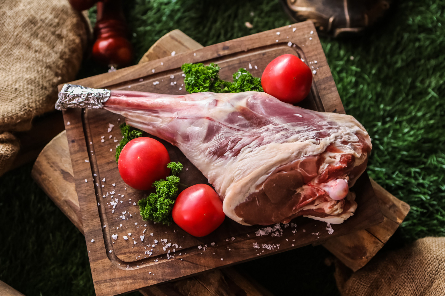 Gigot d’agneau cru avec tomates et persil sur planche rustique chez-basta à muret